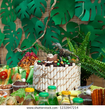 candy bar on children's birthday. cake with dinosaur and sweets, ornaments in green tones