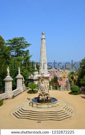 View of the fountain and sculptures on the terrace leading to Shrine of Our Lady of Remedies in Lamego, Portugal. Lamego city and surrounding hilly landscape is in the background. Photo: Sep 2nd 2018