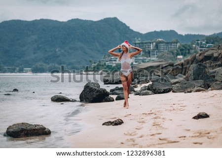 Young woman in white swimsuit and santa hat on tropical beach. Christmas vacation. Woman wearing Santa hat and bikini enjoying christmas on tropical beach. Phuket. Thailand.