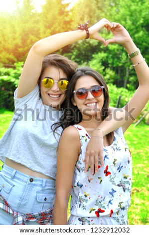 Best friends girls showing heart gesture. lifestyle and people concept: Two young girl hipster friends sisters standing together and having fun. Looking at camera.