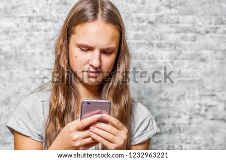 portrait of young teenager brunette girl with long hair using mobile phone on gray wall background