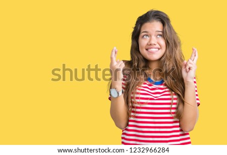 Young beautiful brunette woman wearing stripes t-shirt over isolated background smiling crossing fingers with hope and eyes closed. Luck and superstitious concept.