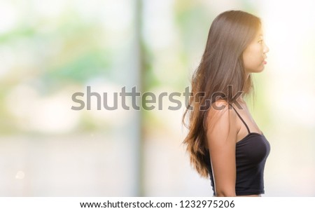 Young asian woman over isolated background looking to side, relax profile pose with natural face with confident smile.