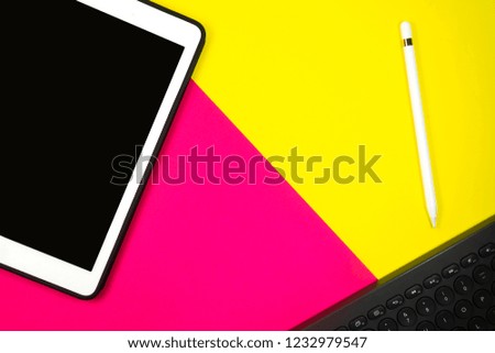 Tablet pencil and keyboard on background two tone with yellow and pink copy space for text