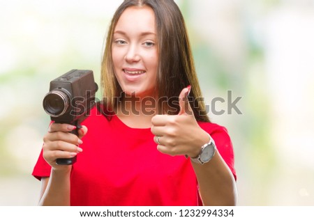 Young beautiful caucasian woman filming using vintage video camera over isolated background happy with big smile doing ok sign, thumb up with fingers, excellent sign