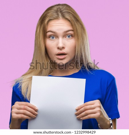 Young caucasian woman holding blank paper sheet over isolated background scared in shock with a surprise face, afraid and excited with fear expression