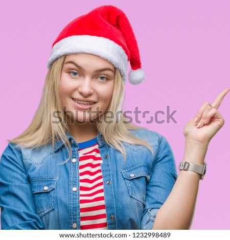 Young caucasian woman wearing christmas hat over isolated background with a big smile on face, pointing with hand and finger to the side looking at the camera.