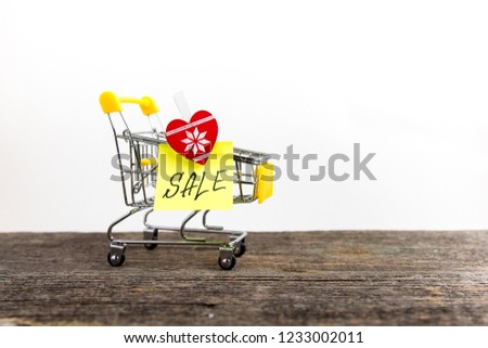 Shopping cart on wooden background with sale sign. Heart shaped clothespin with sale tag. Shopping and commerce concept.