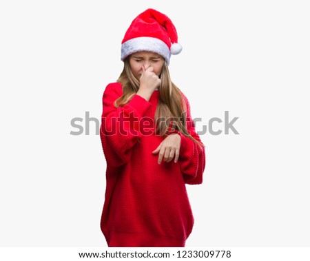 Young beautiful girl wearing christmas hat over isolated background smelling something stinky and disgusting, intolerable smell, holding breath with fingers on nose. Bad smells concept.