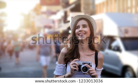 Beautiful young caucasian taking photos in city centre are walking Khaosan Road walking street in evening at Bangkok, Thailand. Happy female traveler and tourist concept.