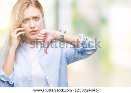 Young blonde woman talking using smarpthone over isolated background with angry face, negative sign showing dislike with thumbs down, rejection concept