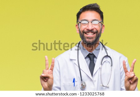 Adult hispanic doctor man over isolated background smiling looking to the camera showing fingers doing victory sign. Number two.