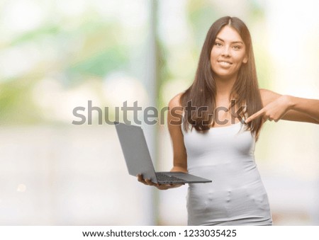 Young hispanic woman using computer laptop with surprise face pointing finger to himself