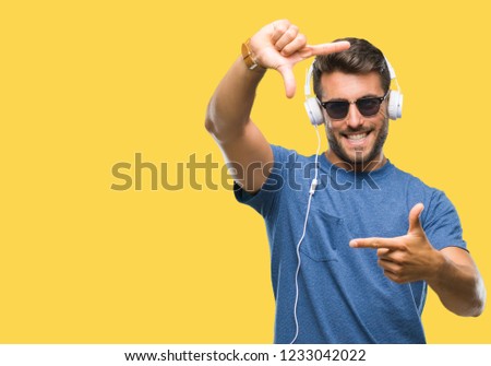 Young handsome man wearing headphones listening to music over isolated background smiling making frame with hands and fingers with happy face. Creativity and photography concept.