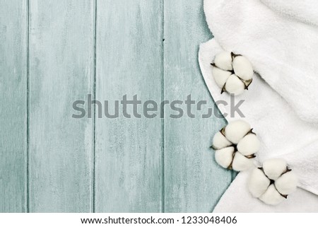 White fluffy towel with cotton boll flowers over a blue green background. Image shot from an overhead top view with free space for text.   