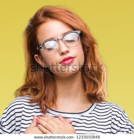 Young beautiful woman over isolated background wearing glasses smiling with hands on chest with closed eyes and grateful gesture on face. Health concept.