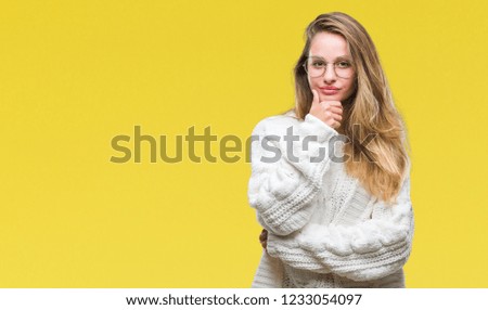 Young beautiful blonde woman wearing winter sweater and sunglasses over isolated background looking confident at the camera with smile with crossed arms and hand raised on chin. Thinking positive.