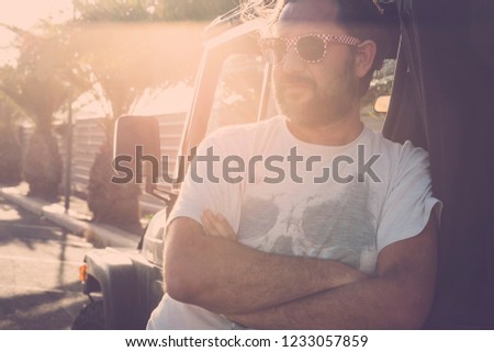 Man middle age with sunglasses standing near off road car parked in tropical street with sun in backlight - sunset atmosphere for nice caucasian people - travel concept