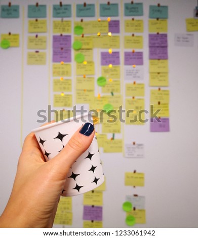 A woman handholding cartoon coffee cup in front of an agile board with colorful cards