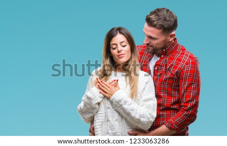 Young couple in love wearing winter sweater over isolated background smiling with hands on chest with closed eyes and grateful gesture on face. Health concept.