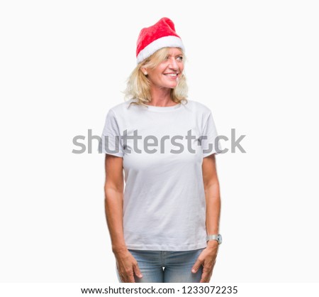 Middle age blonde woman wearing christmas hat over isolated background looking away to side with smile on face, natural expression. Laughing confident.
