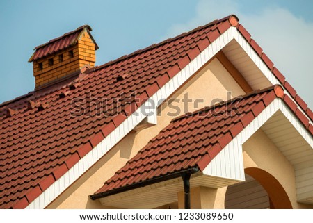 Top detail of big modern expensive residential cottage with steep shingled roof, brick chimney, stucco walls on blue sky background. Construction, professional roofing and investment concept.