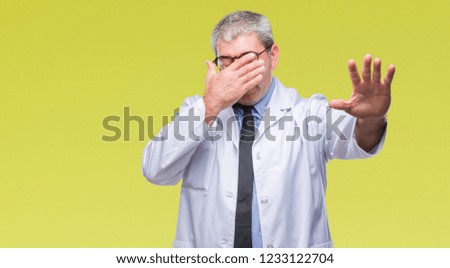 Handsome senior doctor, scientist professional man wearing white coat over isolated background covering eyes with hands and doing stop gesture with sad and fear expression. Embarrassed and negative