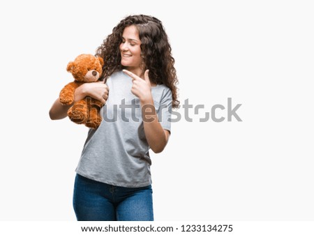 Young brunette girl holding teddy bear over isolated background very happy pointing with hand and finger