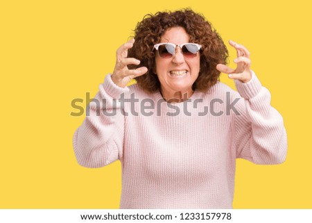 Beautiful middle ager senior woman wearing pink sweater and sunglasses over isolated background Shouting frustrated with rage, hands trying to strangle, yelling mad