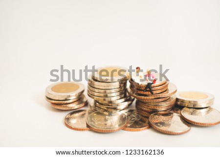 Miniature people man and woman sitting on stack coins isolate on white background using as business and finance concept