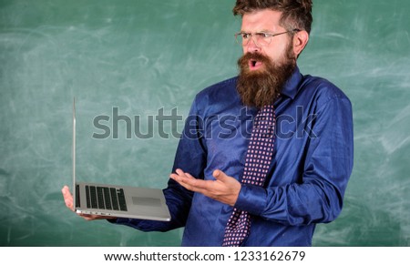 Teacher bearded man confused work with modern laptop chalkboard background. Hipster teacher confused expression holds laptop. Distance education issues. Teaching issues using modern technologies.