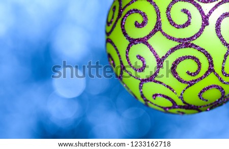 Festive decoration for Christmas tree, green ball with glitter decor on blue blurred background, close up. Christmas decoration or toy for Christmas tree with shimmering details. Ornament concept.