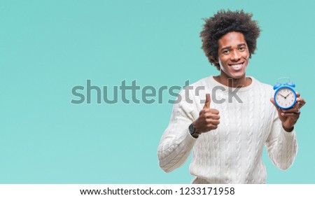 Afro american man holding vintage alarm clock over isolated background happy with big smile doing ok sign, thumb up with fingers, excellent sign