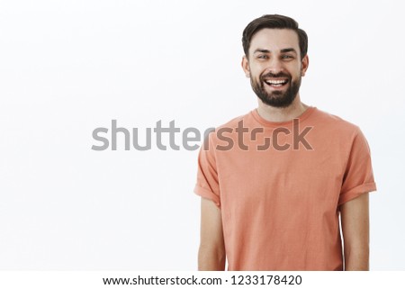 Waist-up shot of bright and cheerful emotive friendly bearded 30s man with broad smile gazing satisfied and upbeat at camera as posing in pink t-shirt over gray background, amused and enthusiastic