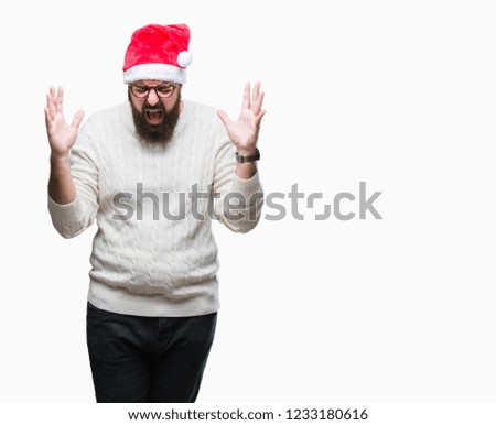 Young caucasian man wearing christmas hat and glasses over isolated background celebrating mad and crazy for success with arms raised and closed eyes screaming excited. Winner concept