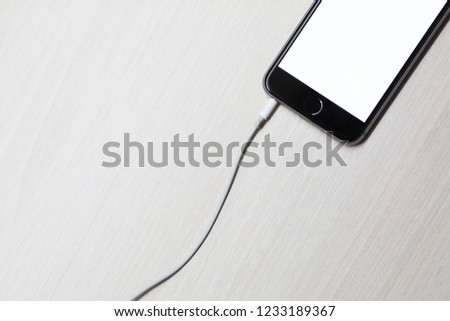 Smartphone with mockup screen and cable from charging on white wooden table background