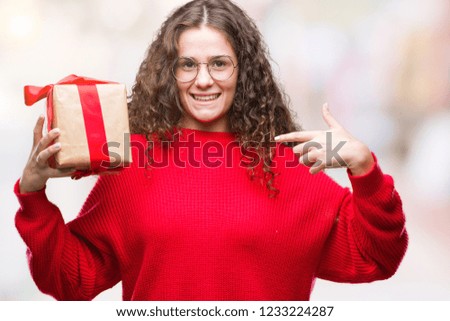 Young brunette girl holding a gift over isolated background with surprise face pointing finger to himself