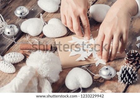 Girl sitting at her desk cutting snowflake for Christmas decor. Closeup of hands on dark wooden background