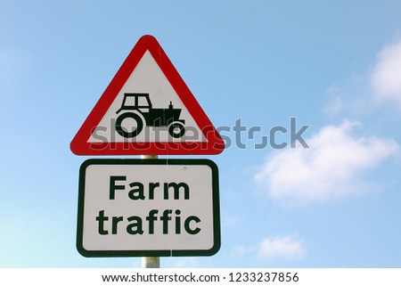 Triangle Road sign with tractor and text Farm traffic, blue cloudy sky