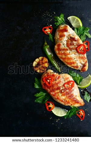 Roasted spicy chicken fillet with greens and vegetables on a black metal, slate or concrete background.Top view with copy space.Rustic style.