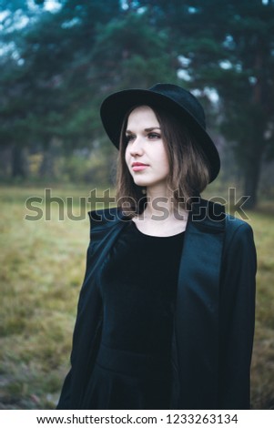 Portrait of a beautiful girl in a black hat in the gloomy autumn forest