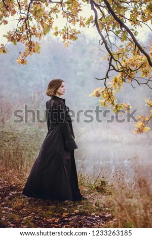 Woman in a long black coat over a cliff above the river