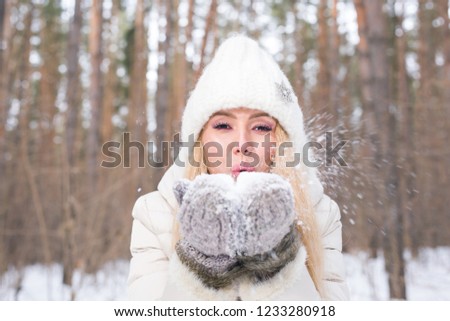 Christmas, holidays and season concept - Young happy blond woman blowing snow in the winter nature