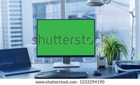 Shot of the Office Desk with Green Mock-up Screen Personal Computer Standing on it. Modern Stylish Room with a Big City Business District View.