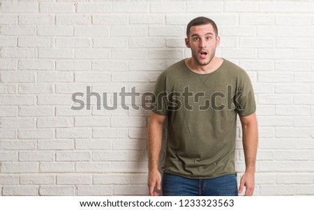 Young caucasian man standing over white brick wall afraid and shocked with surprise expression, fear and excited face.