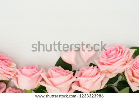 Rose fresh flowers border with two Valentines day hearts on light table from above with copy space, flat lay scene