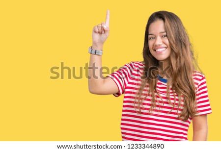 Young beautiful brunette woman wearing stripes t-shirt over isolated background pointing finger up with successful idea. Exited and happy. Number one.