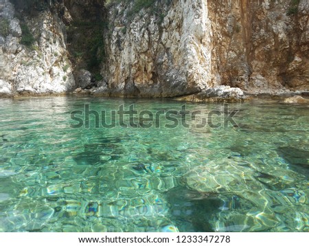 Rocky Beach, with shallow turquoise sea, bellow stony cliffs picture taken from sea level