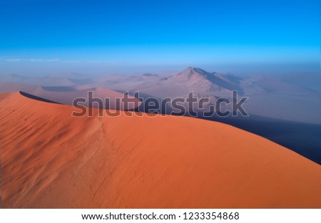 Panoramic, aerial, artistic photo of Namib dunes.  Early morning Namib desert covered in mist. Orange dunes of Namib from above. Desert landscape. Sunrise in Namib-Naukluft  desert. Traveling Namibia.