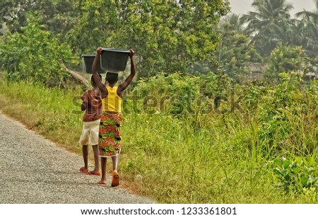 African teenagers carry a luggage on their heads. Young African girls walk along the road. Countryside. Lifestyle in developing countries of Africa. Ghana. Royalty-Free Stock Photo #1233361801